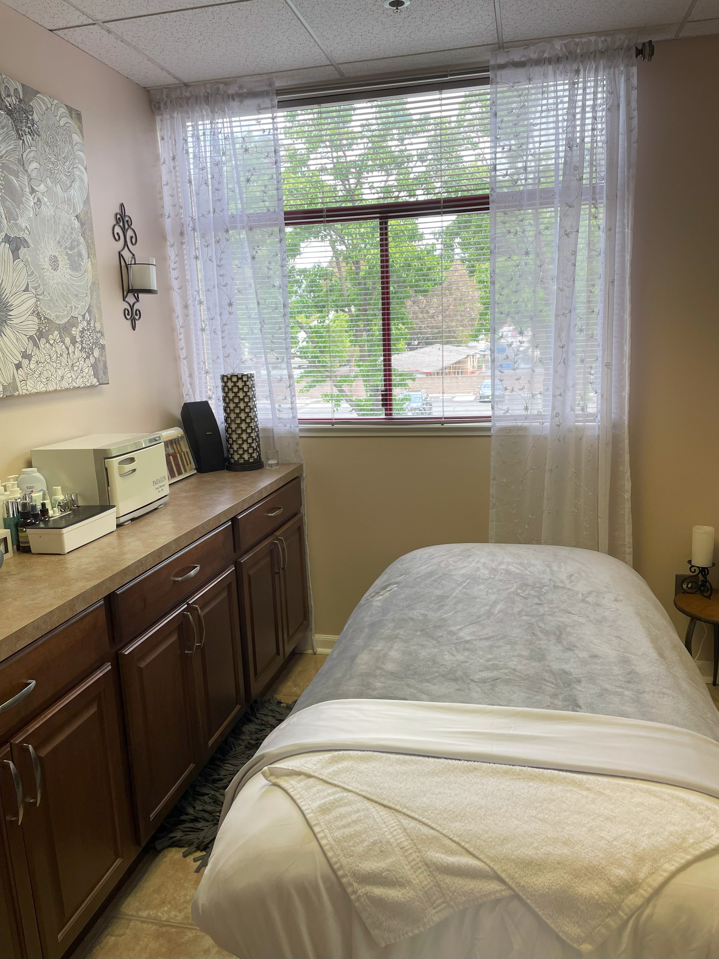 Relaxing and comfortable facial bed with soft gray blanket in a treatment room with natural light coming through the window with green lovely trees in the background