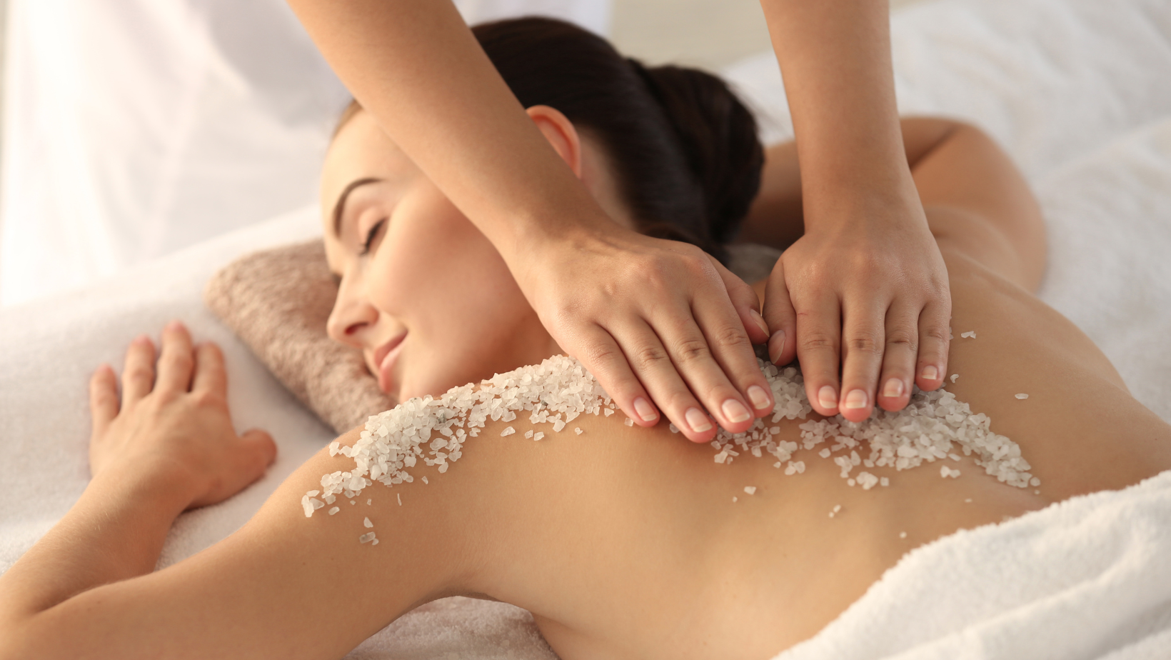 A relaxed woman is receiving a back treatment that includes a salt scrub and wonderful massage from a skilled Esthetician.