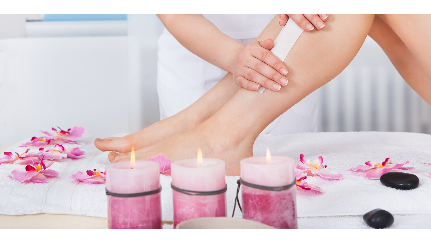 Leg waxing in a serene environment with pink candles and orchid flowers from a skilled Esthetician